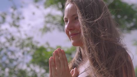 atractiva joven mujer rubia sonriendo con las manos entrelazadas y el viento soplando más allá del cabello