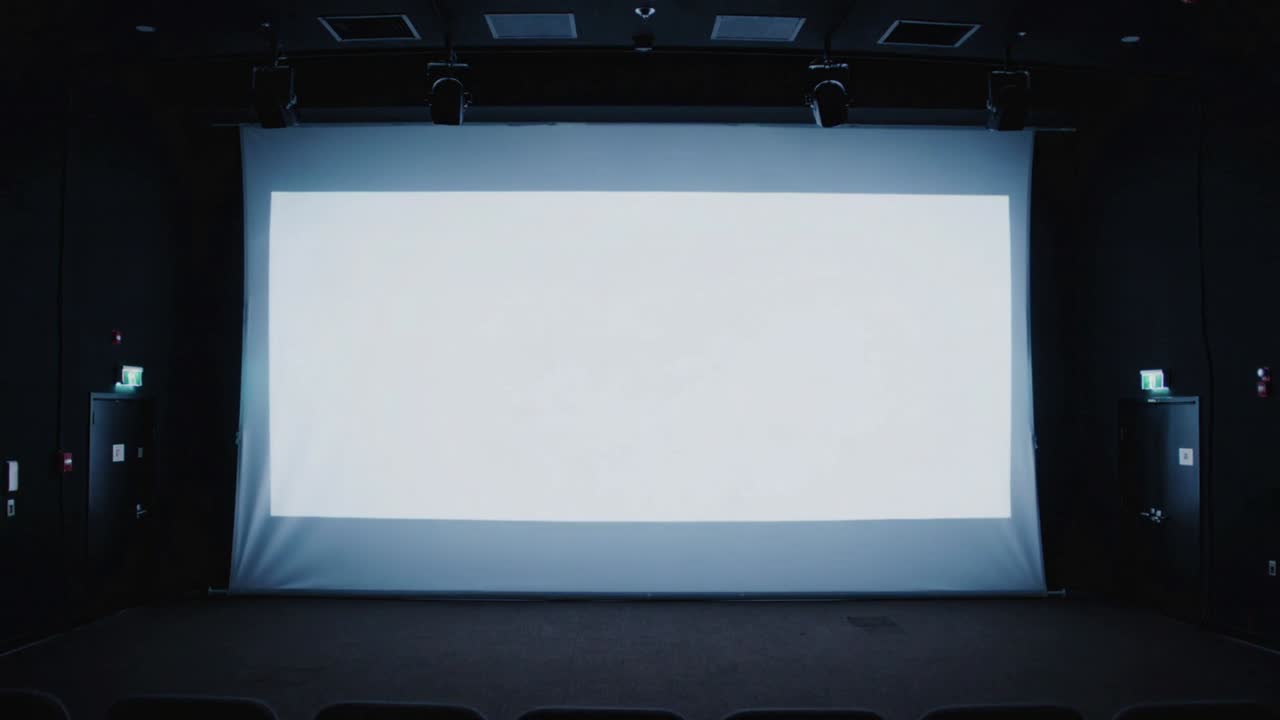 Lampada del proiettore che si affievolisce, causando lo sbiadimento dello schermo di proiezione a teatro, segnalando la fine dello spettacolo, con le file di sedie.