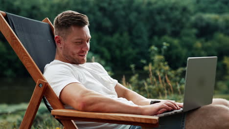 joyful smiling caucasian man works on laptop. freelance businessman working remotely in nature.