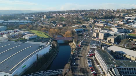 Filmische-Drohnenaufnahmen-Aus-Der-Luft-Einer-Kleinstadt-In-England,-Die-Eine-Zweispurige-Straße,-Einen-Breiten-Fluss-Und-Eine-Geschäftige-Stadt-Mit-Verkehr-Und-Straßen-Zeigen