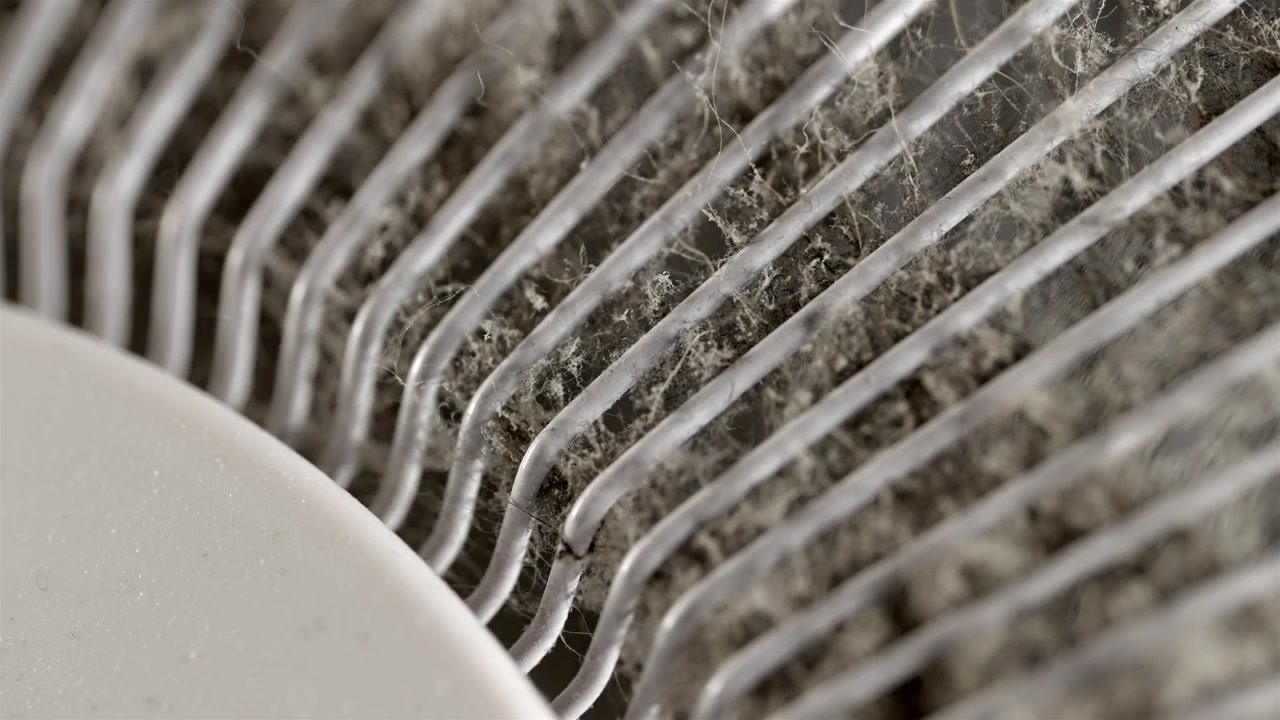 Staubiges weißes oszillierendes Ventilatorgitter füllt den Rahmen bei sanftem Innenlicht.