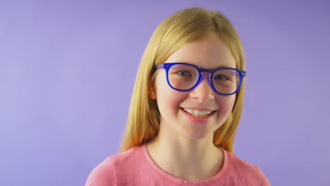 fotografía de estudio de una chica sonriente con cabello largo que usa gafas azules contra un fondo púrpura