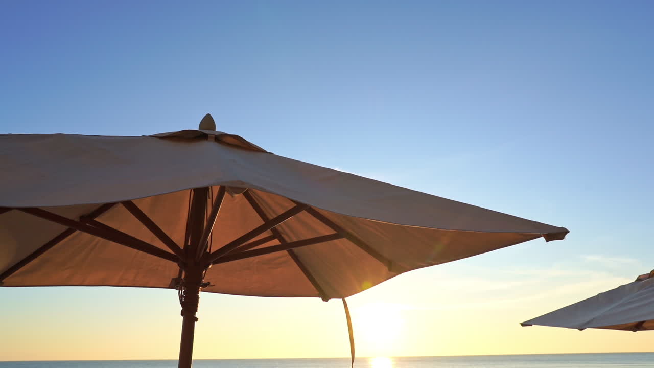 Low angle view of parasols and palm trees under evening sun in backlight. Exotic luxury vacation concept