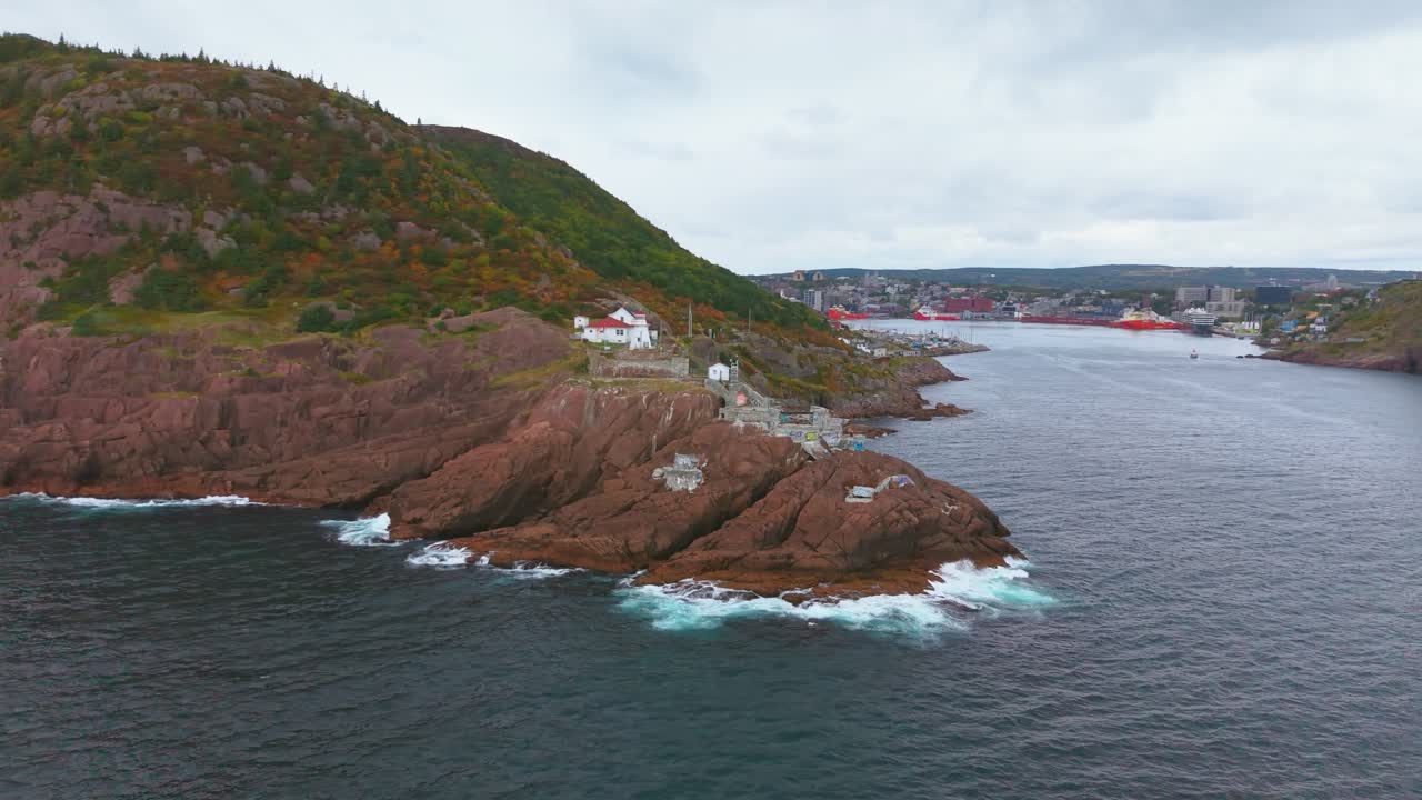 Cinematic drone footage captures Fort Amherst’s quiet inlet and sloping hills dotted with pastel homes, where rocky terraces meet a calm harbor and waves gently break along the shoreline