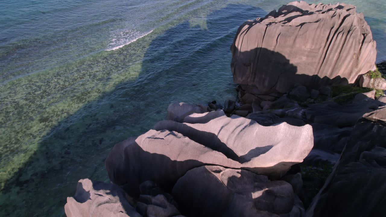 Luftfoto, der glider over skulpturerede granitblokke for at afsløre det krystalklare turkisblå vand og koralrevene ved Anse Grosse Roche på La Digue-øen, Seychellerne. 013