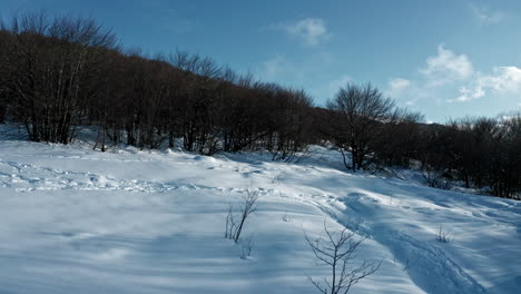 A-snow-covered-mountain-with-cable-cars-and-sun-peeking-over-the-ridge,-aerial-view