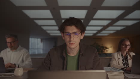 young focused man working on laptop during evening in office