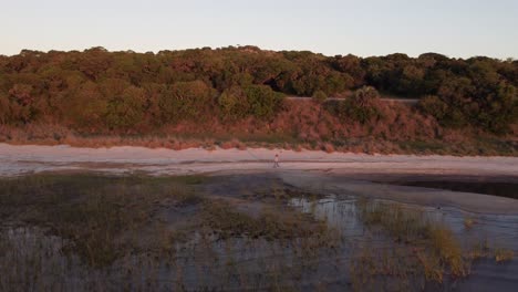 Rothaarige-Frau-Hält-Ihr-Mobiltelefon-In-Der-Hand,-Während-Sie-In-Der-Abenddämmerung-Am-Sandstrand-Von-Laguna-Negra-In-Uruguay-Spaziert