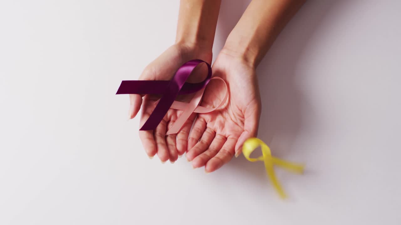 Video di mani di donna caucasica che tiene nastri viola e rosa su sfondo bianco