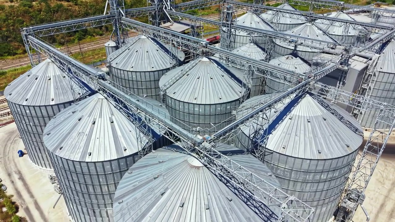 Farm with many grain silos and structures near train tracks during daylight