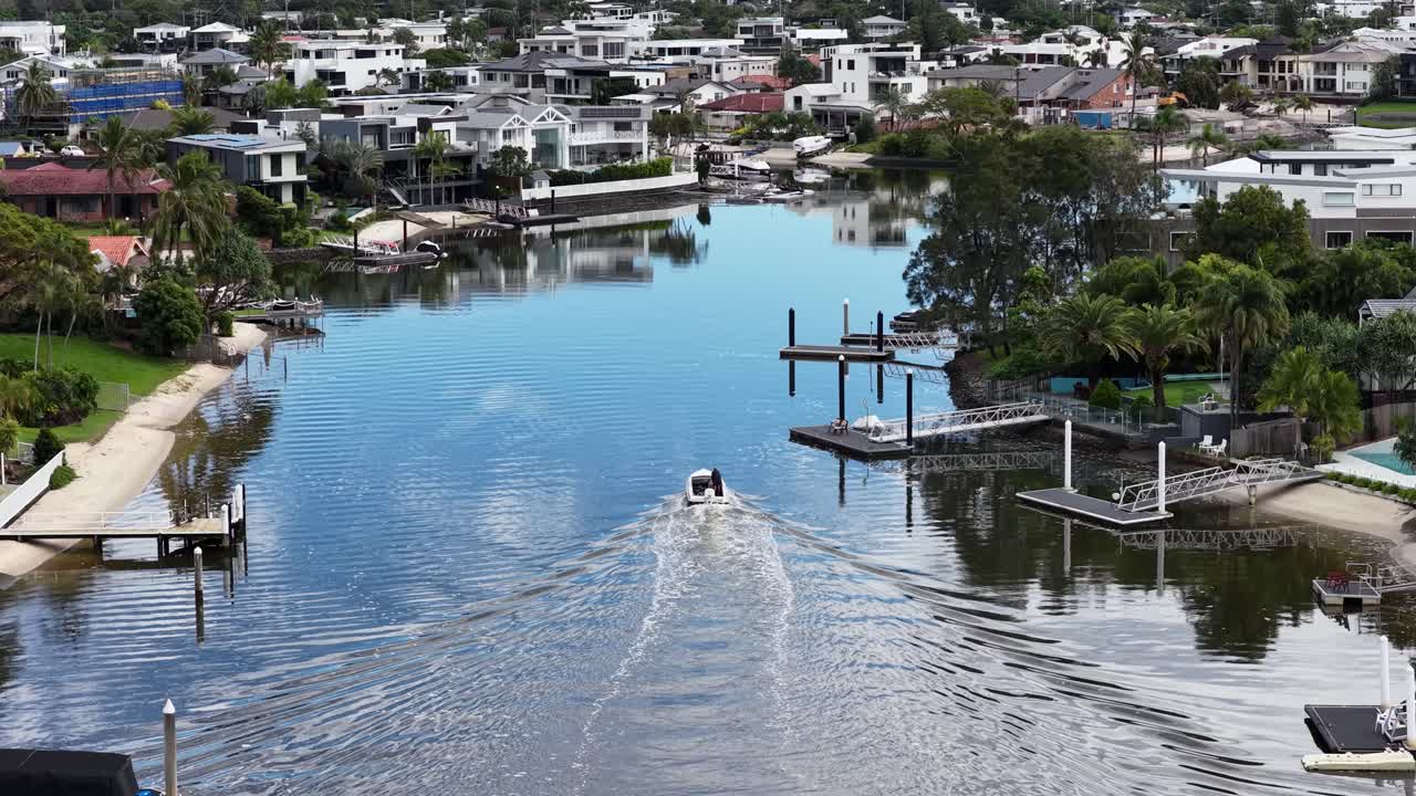 A boat glides through Gold Coast canals, surrounded by luxury homes and lush greenery under clear skies