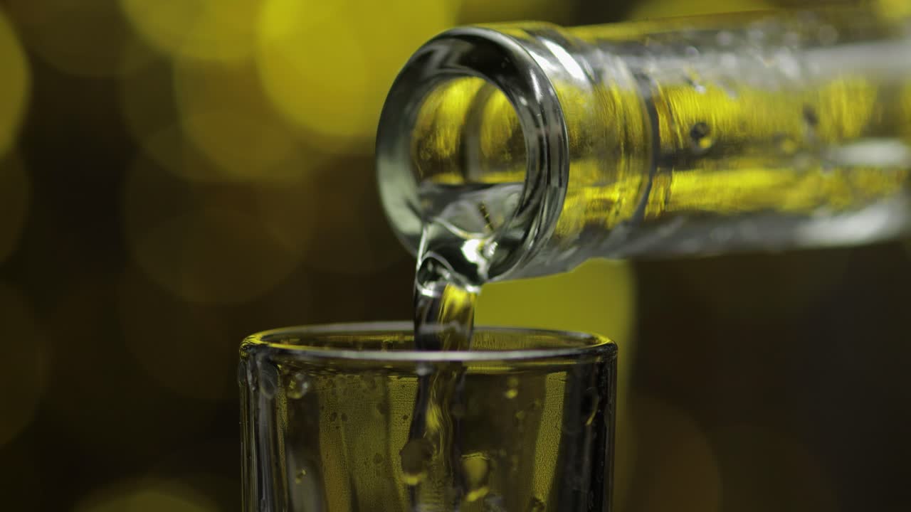 el camarero vierte vodka congelada de la botella en un vaso contra el brillante fondo de celebración de la fiesta de oro