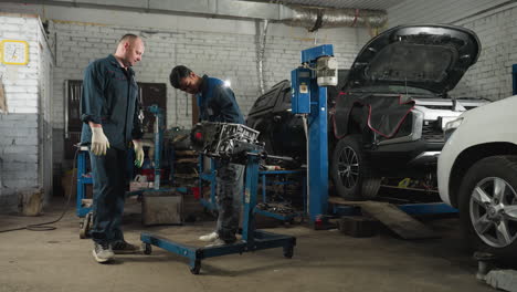ingenieros mecánicos en un taller de automóviles, uno con guantes rojos trabajando en un motor de coche mientras el colega observa, el fondo presenta coches estacionados, herramientas y equipos de taller