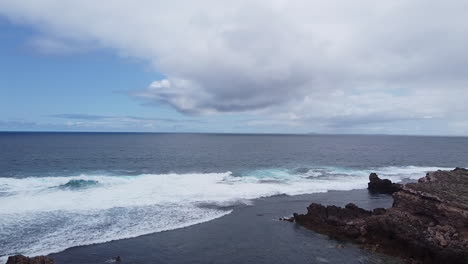 A-rough-coastline-with-sizable-waves,-a-layered-rock-shelf,-and-a-cliff-that-descends-to-a-peaceful-bay