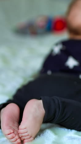 tiny baby lies on his belly and looks at the toy in front of him. little bare baby feet close up. white blurred backdrop. vertical video