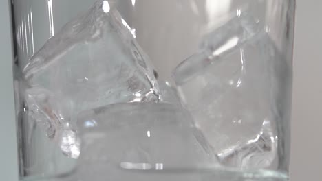 macro ice cubes in clear tall class have clear liquid poured in slow motion 4k