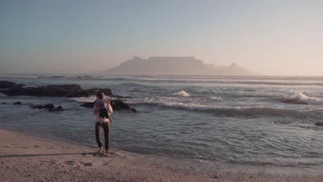 playful mother lifts her son and twirls him around on beach as sun sets, creating joyful and heartwarming moment against backdrop of clear blue sky