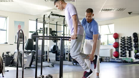 using parallel bars for rehabilitation exercise, man with disability supported by therapist