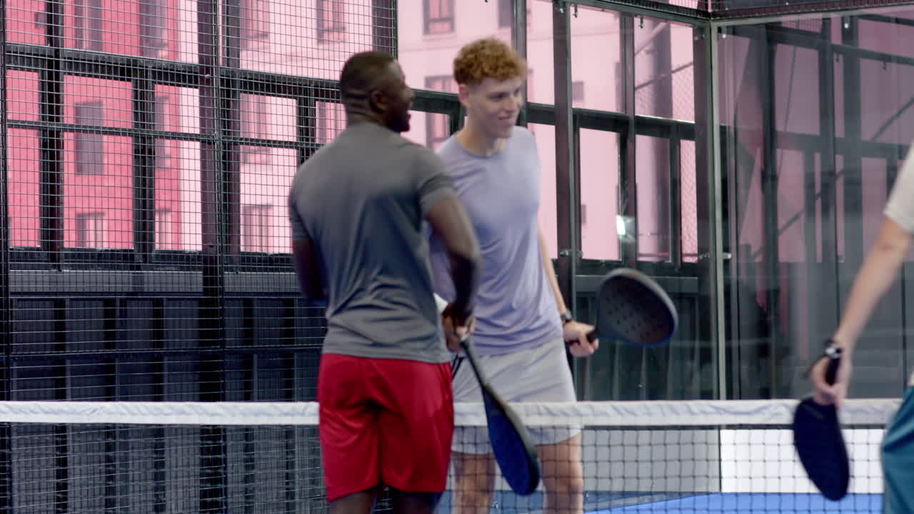 Young diverse men enjoying padel tennis match, laughing and supporting each other, on indoor court