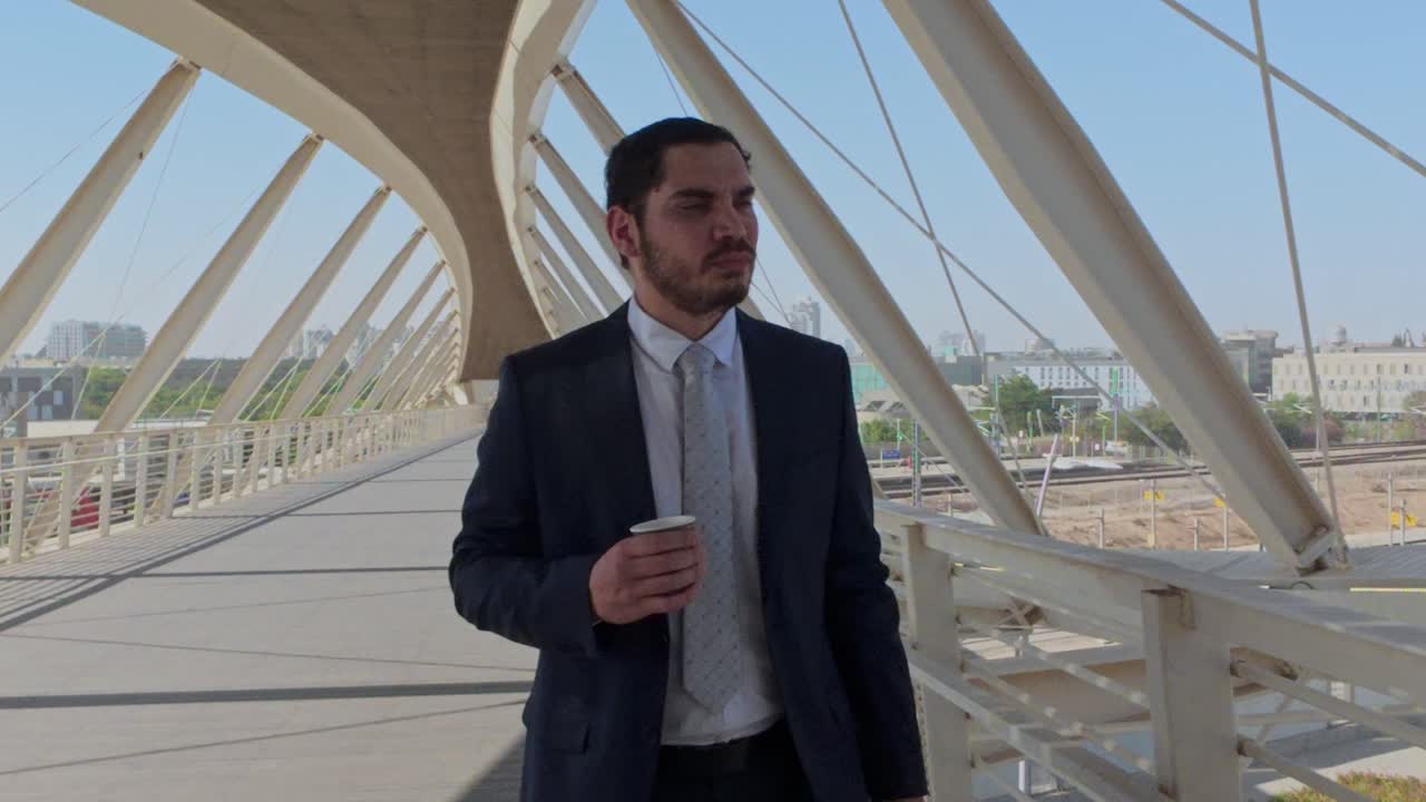 Businessman Checking His Smartphone While Holding a Coffee on a Bridge