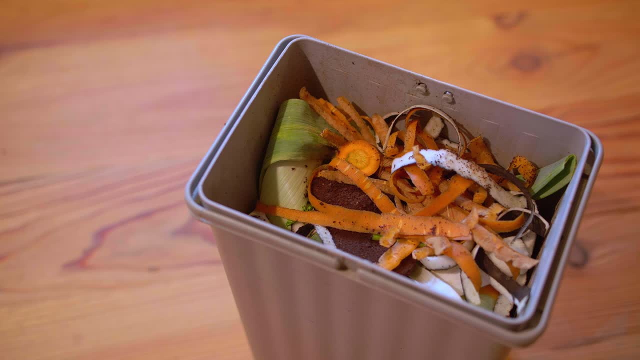 A container filled with organic waste like carrot peels and celery stalks. An eco-friendly habit to reduce waste and help the environment. High-angle shot