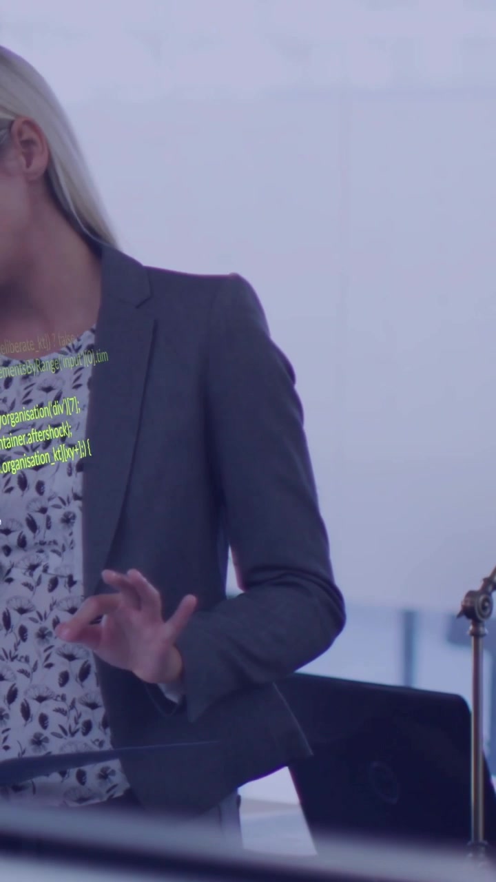 Vertical video: Woman speaking at business meeting, gesturing as laptop showing green code overlay