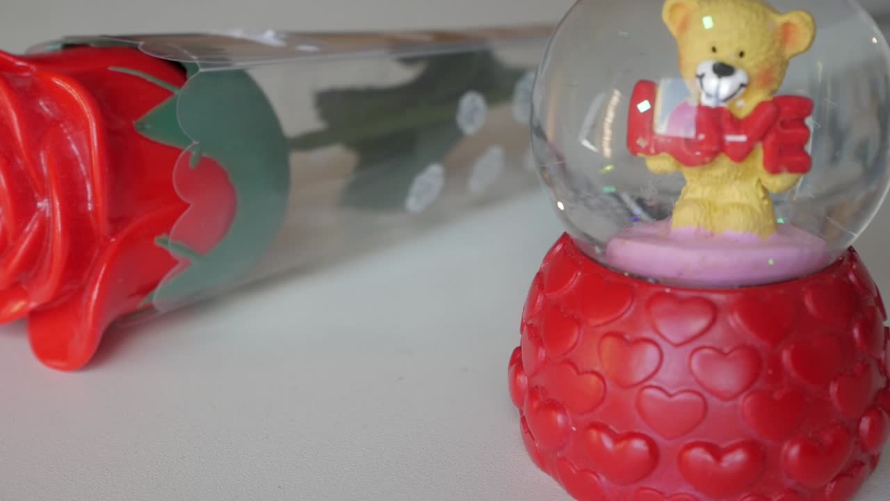 A Valentine’s themed snow globe with a teddy bear holding a “LOVE” sign, and a red rose