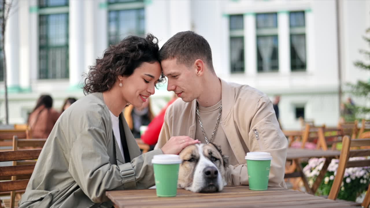 Una coppia felice all'aperto vicino a un bar. Accarezzano il loro cane, caffè sul tavolo. Atmosfera autunnale. Movimento al rallentatore