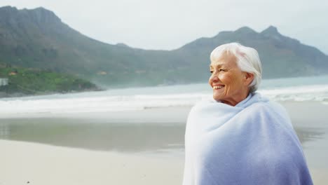 Senior-woman-covering-herself-with-blanket-on-beach