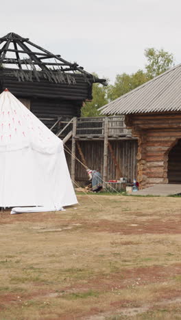 césped frente a una alta valla de madera con arco. patio de la finca del señor feudal. la gente medieval hace tareas domésticas en el territorio del asentamiento y se sienta a la mesa