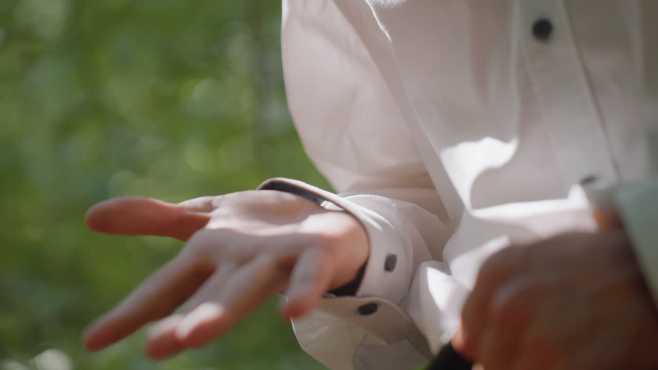 Portrait view of ecologist in white shirt and glasses standing outdoors closely observing his hand palm with gentle smile, sunlight filtering through leaves creating warm natural forest atmosphere