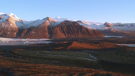 Aerial-extreme-wide-shot-180-degrees-pan-of-rugged-landscape-in-the-Snaefellsjokull-Glacier-in-South-coast-of-Iceland-on-a-sunset-golden-light-bathed-landscape-and-snow-capped-rugged-mountains