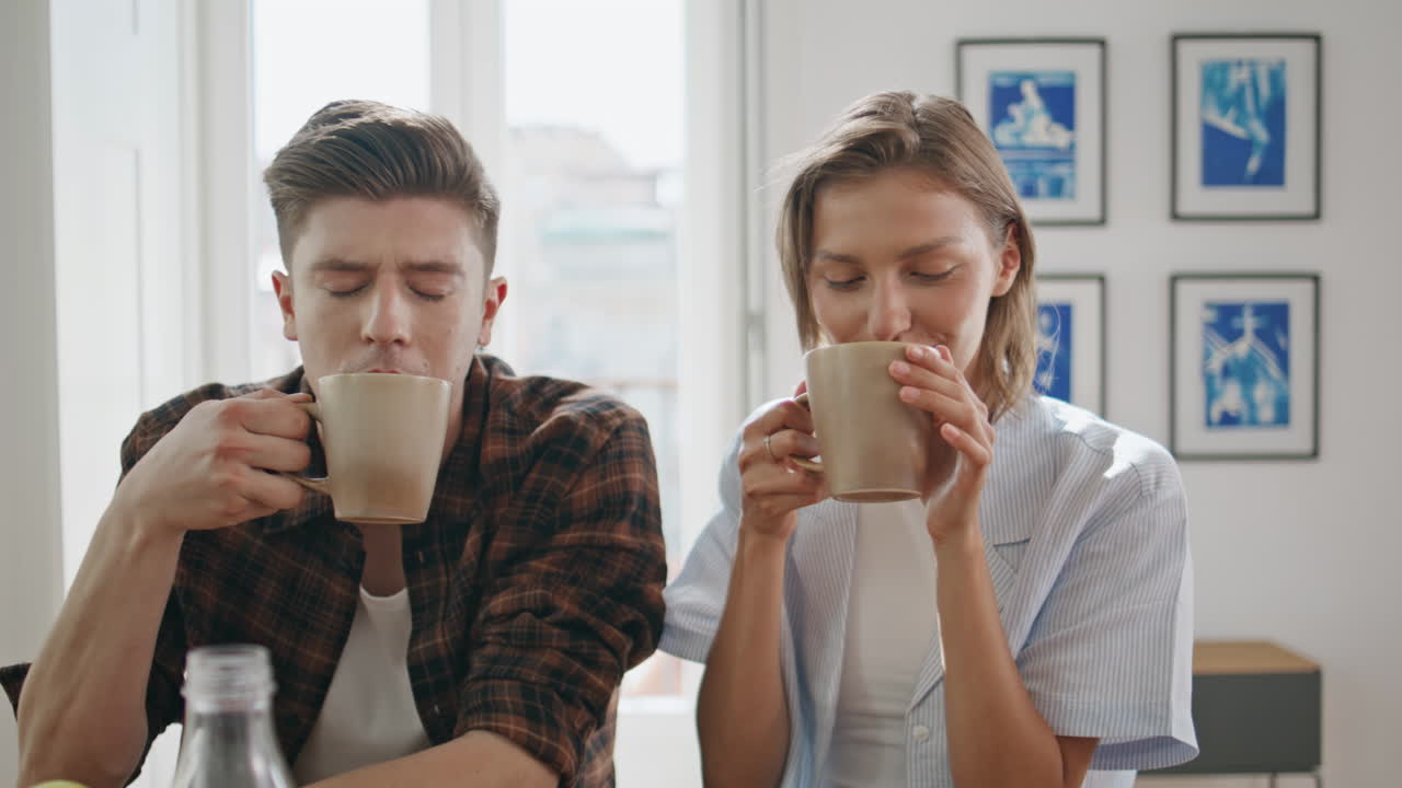 Morning couple sitting together in kitchen closeup. Young family clinking cups