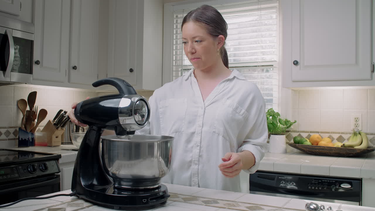 Woman in a white shirt puts a bowl onto an electric mixer in her kitchen