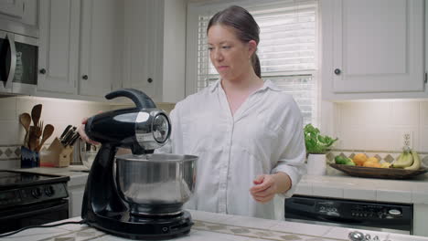 woman in a white shirt puts a bowl onto an electric mixer in her kitchen