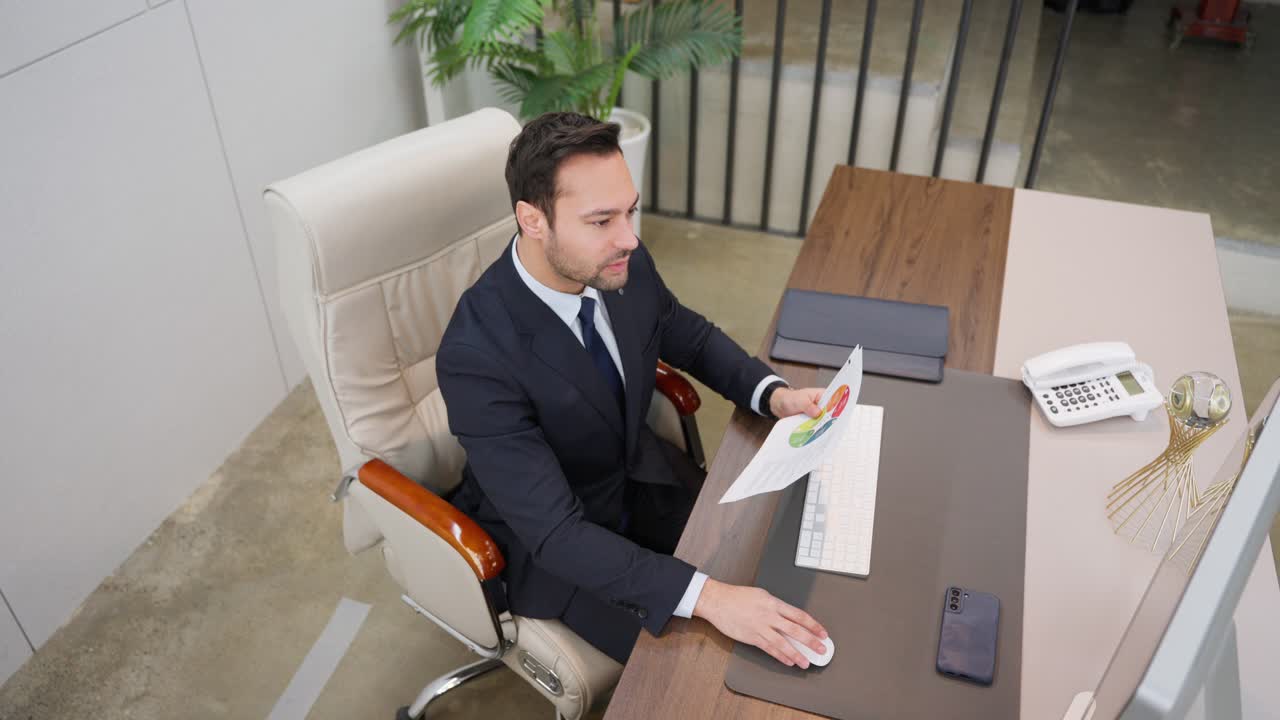 Busy thoughtful European businessman analyzing financial sheet documents checking data on computer while sitting at desk workplace in a business office - high angle top down view