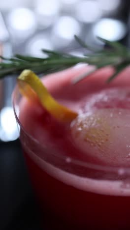 close-up of a red cocktail with rosemary and lemon garnish