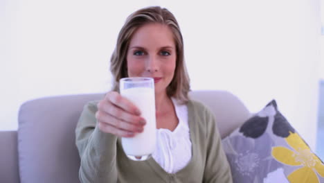 mujer alegre bebiendo un vaso de leche y mostrándolo