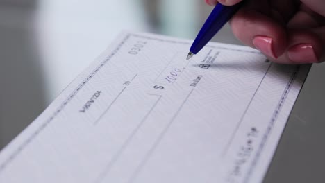 business woman hand signs and filling bank check for one thousand 1000 dollars