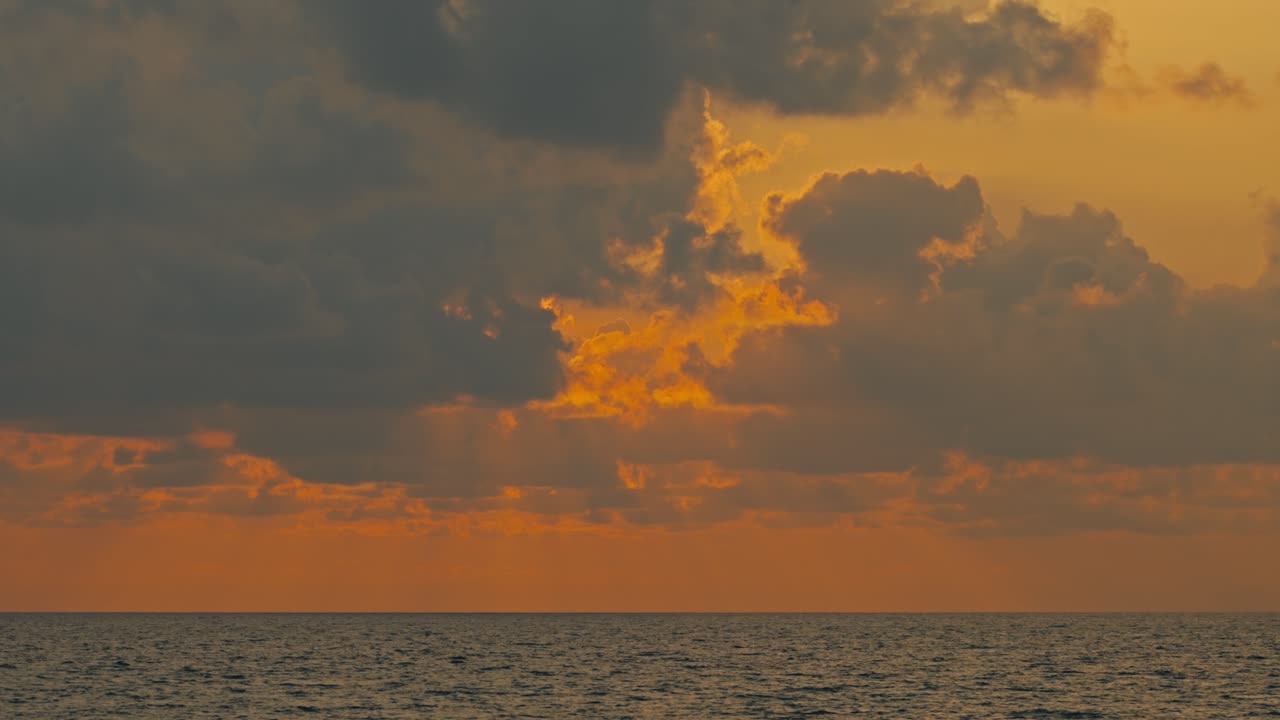 Tief orangeroter Sonnenuntergangshimmel über dem Meer mit dramatischen Wolken, während die Sonne sich hinter der Wolkenschicht verbirgt. Atmosphärische Meereslandschaft mit leuchtendem Licht, ruhigem Horizont und friedlicher Abendstimmung.