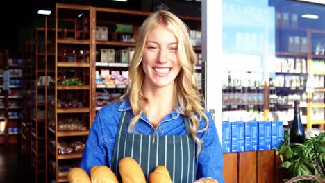 Smiling-woman-holding-a-basket-of-baguettes-in-organic-shop