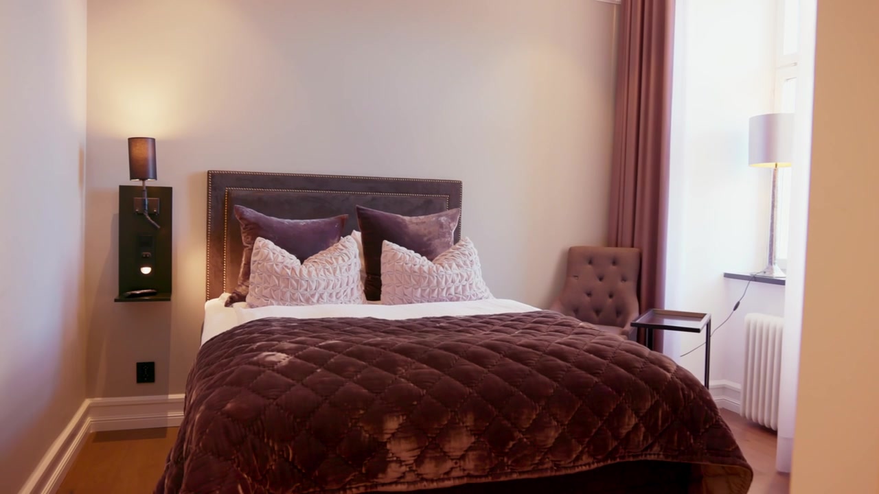 Primo piano di cuscini rosso vino su un letto d'hotel che mostrano colore vibrante, texture ricca, tessuto morbido, creando contrasto con la biancheria bianca e fresca, luce calda che aggiunge profondità, sensazione accogliente ed eleganza lussuosa