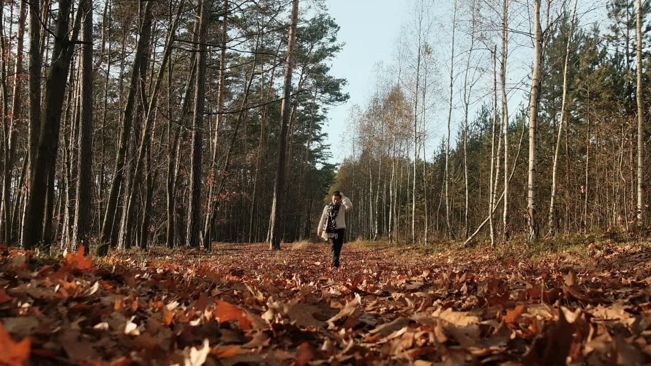 Kvinde går på sti i efterårsskov på en solrig dag, slowmotion