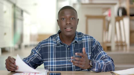 African-american-man-sitting-at-table-holding-documents-and-having-video-call-at-home,-slow-motion