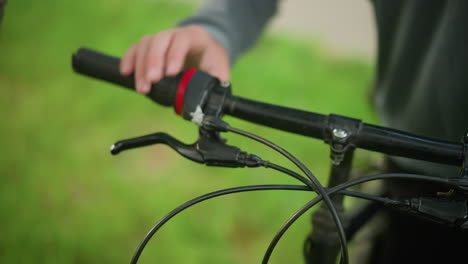 close-up of individual wearing black trousers and grey cloth, approaches parked bicycle, adjusting brake lever in grassy field, the person holds the handlebar with firm grip