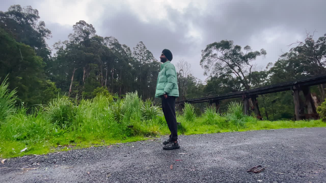 숲에서 주위를 둘러보고 비 아래 서 있는 펀자브어 시크교 남자
