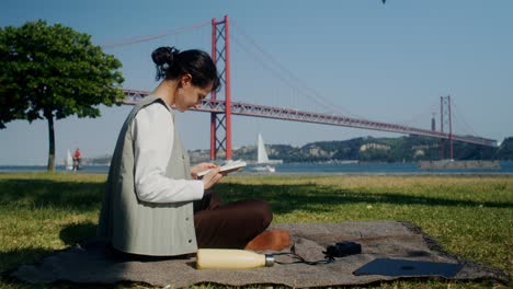 woman reading a book in a park by the bridge