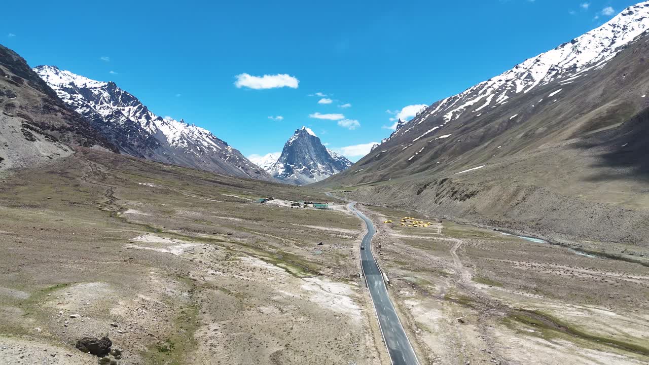 Aerial drone shot following the road that stretches toward the towering peaks of Gombok Ranjan.