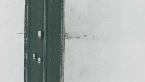 Autos-Fahren-Entlang-Einer-Großen-Grauen-Brücke-über-Einen-Zugefrorenen-Fluss