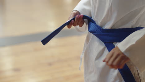 close-up shot of woman standing in gym and tying belt on kimono